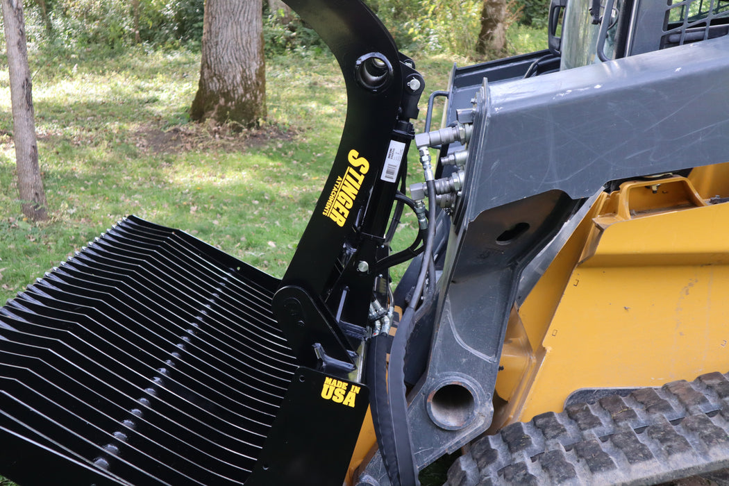 Rugged open-side skid steer grapple bucket by Stinger handling rock piles – versatile tool for contractors, farmers, and land managers.