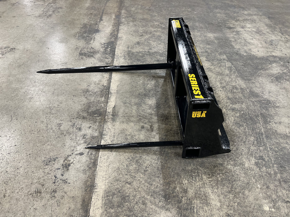 Durable bale spear by Stinger Attachments transporting hay bale on rural farm – rugged design ensures stability and smooth operation in all conditions.
