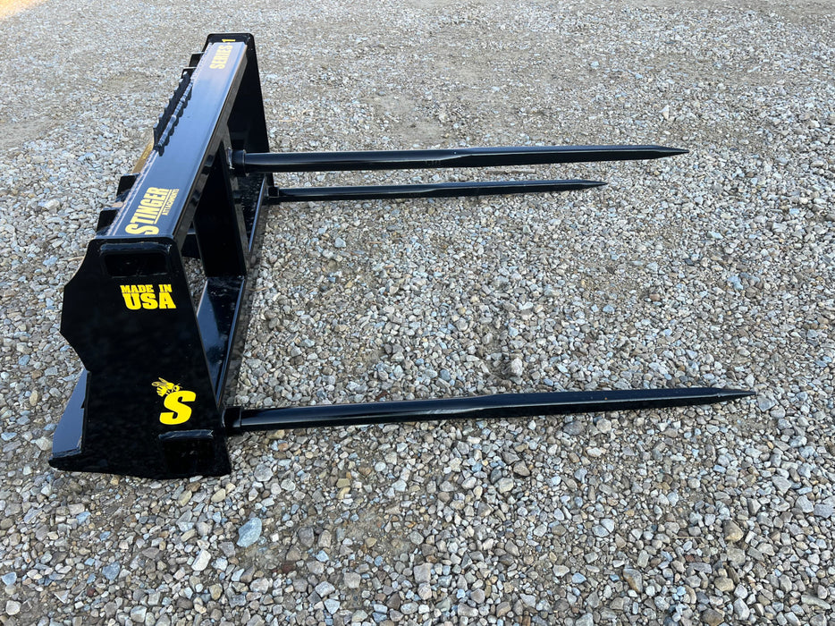 Bale spear by Stinger Attachments lifting round bale on rural property – dependable farm implement for efficient material handling.