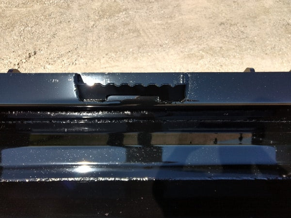 Operator maneuvering Stinger Series 3 skid steer material bucket on uneven terrain – dependable attachment for tough work environments.