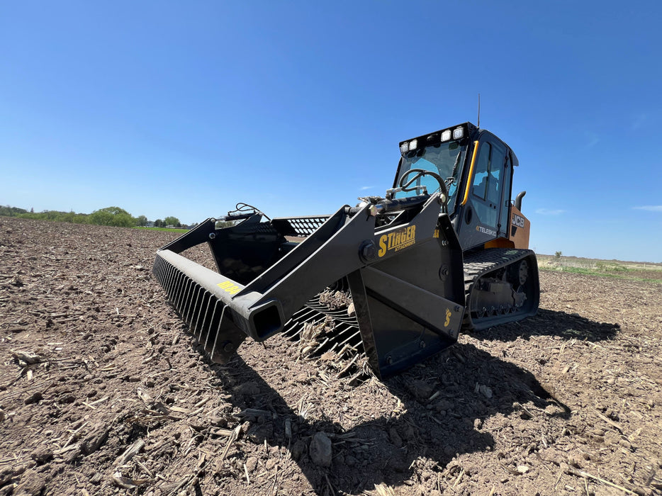 Industrial-grade tractor rock bucket resting on gravel, showcasing durable frame and welded tine design.