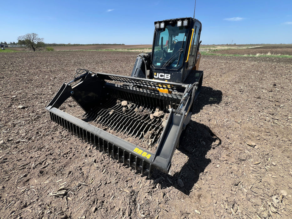 Front angle of the tractor rock bucket attachment highlighting its wide capacity and curved tine structure.