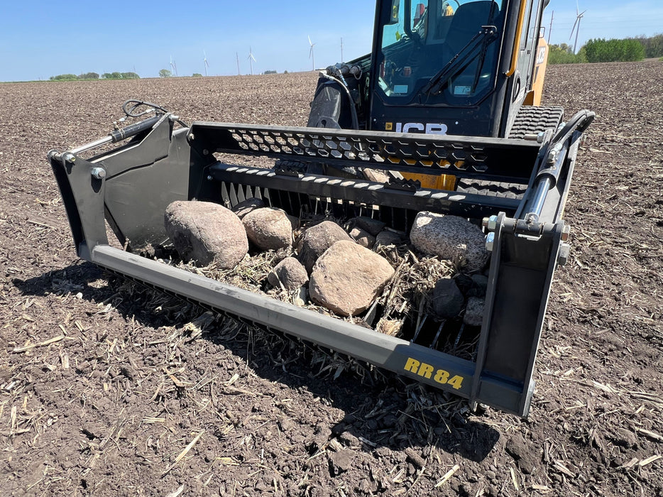 Rear perspective of a tractor rock bucket connected to a front loader with quick-attach system visible.