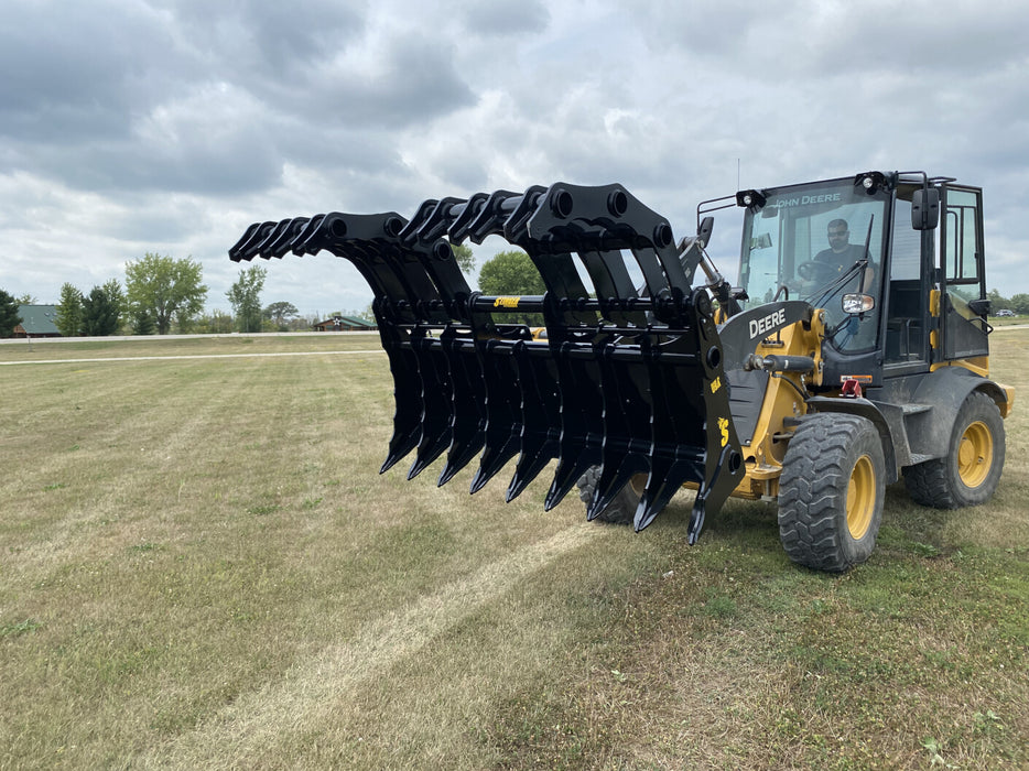 Heavy-duty tractor grapple bucket CG-XD by Stinger Attachments lifting logs and debris on a worksite.