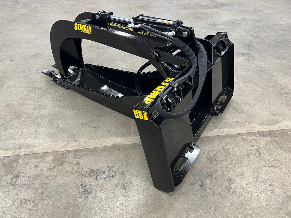 Industrial-grade Stump Grapple Bucket resting on gravel, showcasing its reinforced frame and curved tine design.