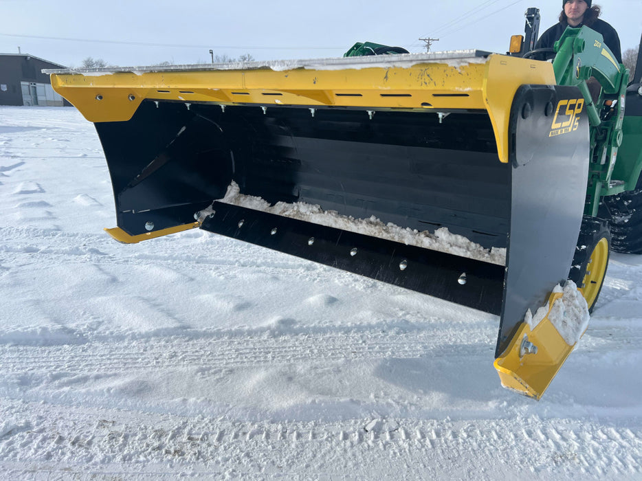 Compact tractor equipped with skid steer snow pusher clearing driveway – strong steel edge provides clean, even snow removal.